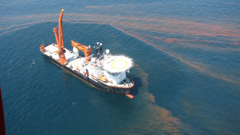 Large vessel in gulf surrounded by oil slick.